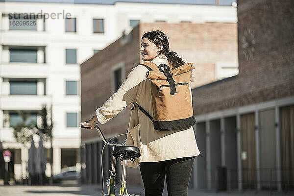 Junge Frau  die einen Rucksack trägt  während sie mit dem Fahrrad auf einer Straße in der Stadt spazieren geht
