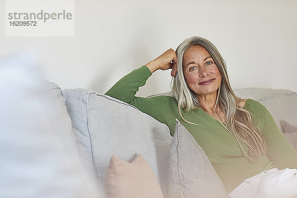 Lächelnde Frau sitzt zu Hause auf dem Sofa