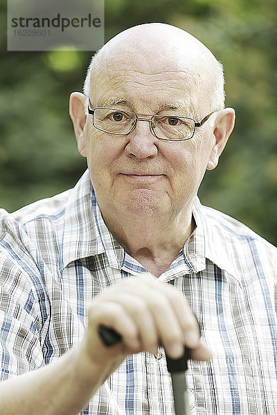 Deutschland  Nordrhein-Westfalen  Köln  Porträt eines älteren Mannes mit Stock im Park  lächelnd