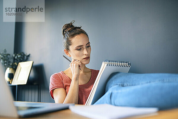 Geschäftsfrau mit Notizblock und Bleistift  die sich am Schreibtisch im Heimbüro ausruht