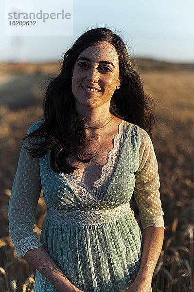 Lächelnde junge Frau mit langen Haaren auf einem Bauernhof bei Sonnenuntergang