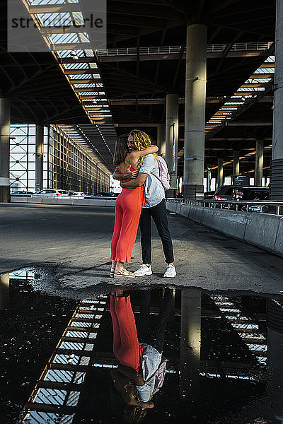 Paar umarmt einander mit Reflexion auf Pfütze in der Stadt