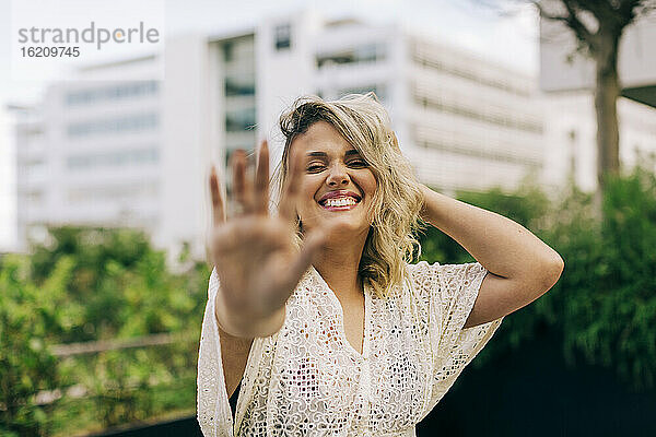 Lächelnde junge Frau mit Hand im Haar  die eine Stopp-Geste zeigt