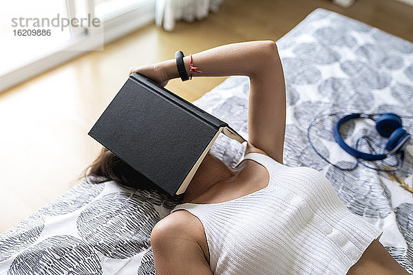 Mittlere erwachsene Frau mit Buch auf dem Gesicht entspannt im Schlafzimmer zu Hause