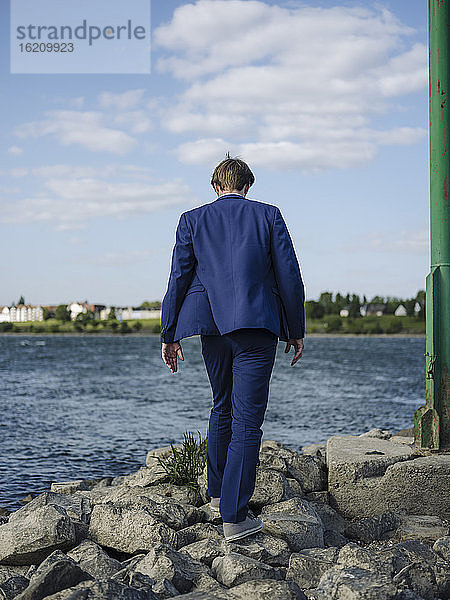 Geschäftsmann im Anzug geht auf Felsen am Rheinufer gegen den Himmel