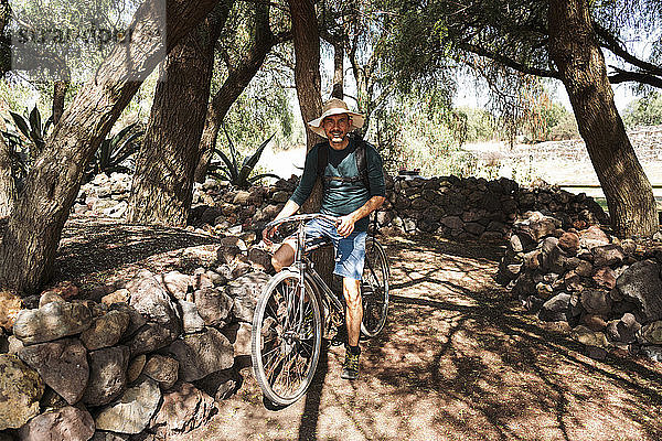 Älterer Mann mit Hut fährt Fahrrad auf einer unbefestigten Straße in Teotihuacan  Mexiko