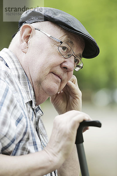 Deutschland  Nordrhein-Westfalen  Köln  älterer Mann mit Mütze und Brille im Park  Nahaufnahme