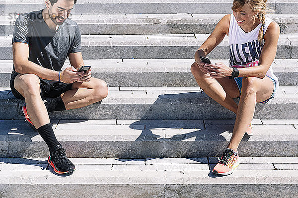 Ein Paar benutzt sein Smartphone auf einer Treppe in der Stadt an einem sonnigen Tag