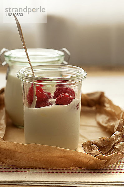 Glas Joghurt mit Himbeeren auf Holztisch  Nahaufnahme