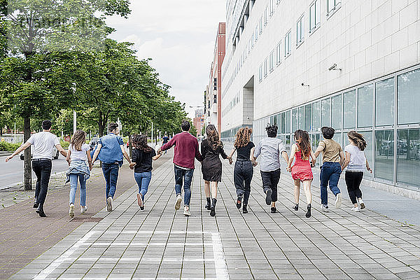 Männliche und weibliche Freunde halten sich an den Händen und laufen auf einem Fußweg in der Stadt