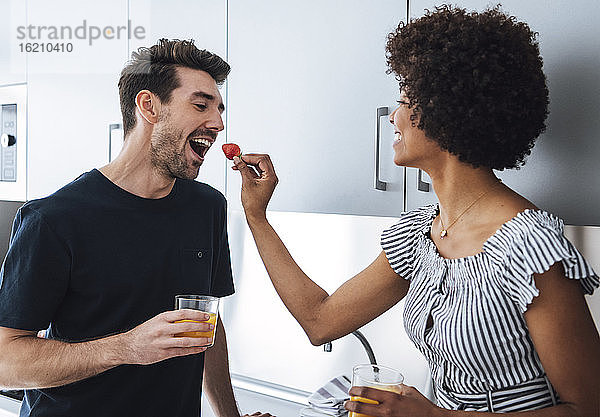 Glückliche Frau füttert Mann in der Küche eines Penthouses mit Erdbeeren