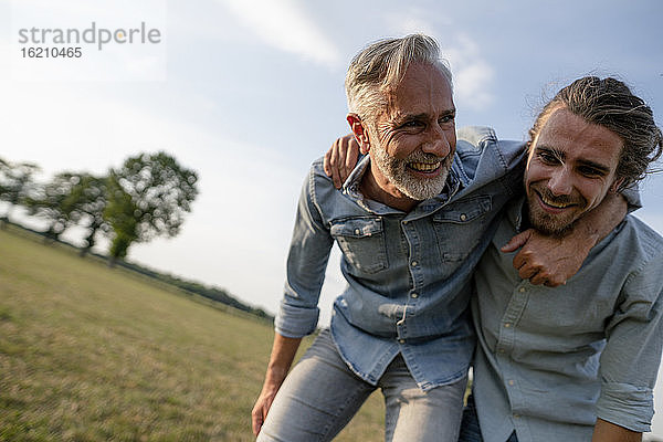Glücklicher Vater und erwachsener Sohn spielen auf einer Wiese auf dem Lande miteinander