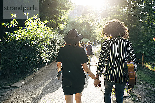 Paar hält sich an den Händen  während es auf dem Fußweg im Park spazieren geht
