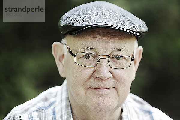 Deutschland  Nordrhein-Westfalen  Köln  Porträt eines älteren Mannes mit Mütze und Brille im Park  lächelnd