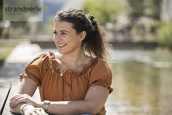Lächelnde junge Frau  die wegschaut  während sie an einem sonnigen Tag im Park sitzt