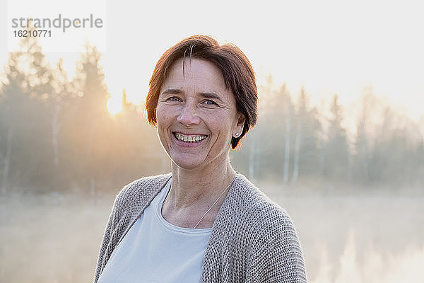 Porträt einer erwachsenen Frau  die bei nebligem Sonnenaufgang in die Kamera lächelt