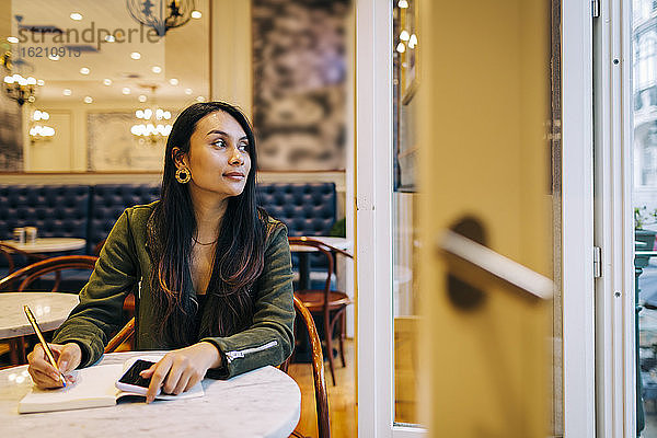 Junge Frau  die im Café in ein Buch schreibt und nach draußen schaut
