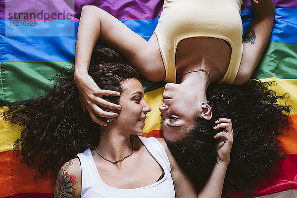 Romantisches lesbisches Paar  das sich gegenseitig anschaut  während es auf der Regenbogenflagge liegt