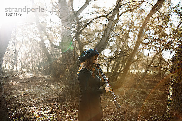 Junge rothaarige Frau spielt Klarinette beim Üben im Wald