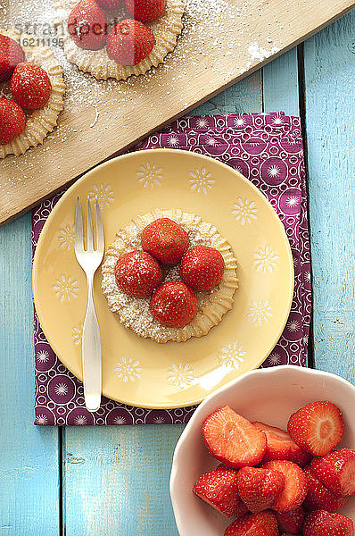 Erdbeertörtchen auf Teller neben Schale mit Erdbeeren  Nahaufnahme