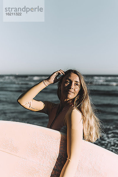 Junge Frau mit Surfbrett  die wegschaut  während sie auf dem Meer steht
