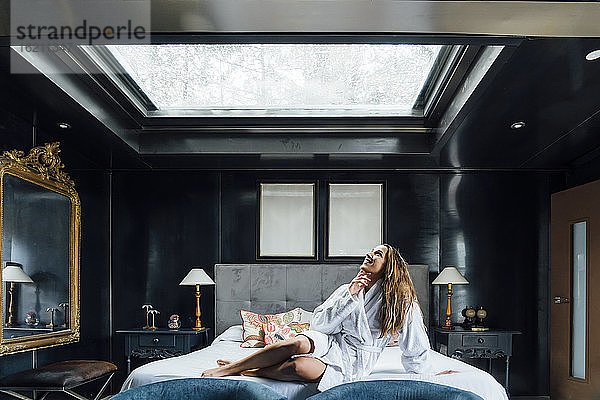 Mittlere erwachsene Frau schaut durch ein Oberlicht  während sie sich auf einem Hotelbett entspannt