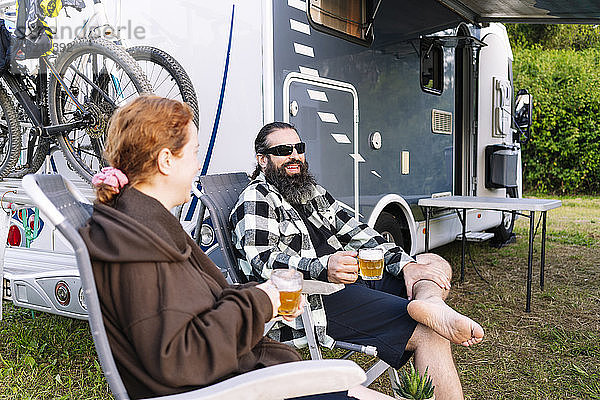 Entspanntes Paar sitzt neben dem Wohnmobil und genießt den Urlaub und trinkt Bier