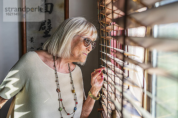 Ältere Frau mit Sonnenbrille schaut durch ein Fenster zu Hause