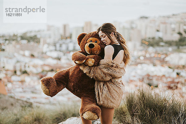 Frau mit geschlossenen Augen  die einen Teddybär umarmt  während sie vor der Stadt steht