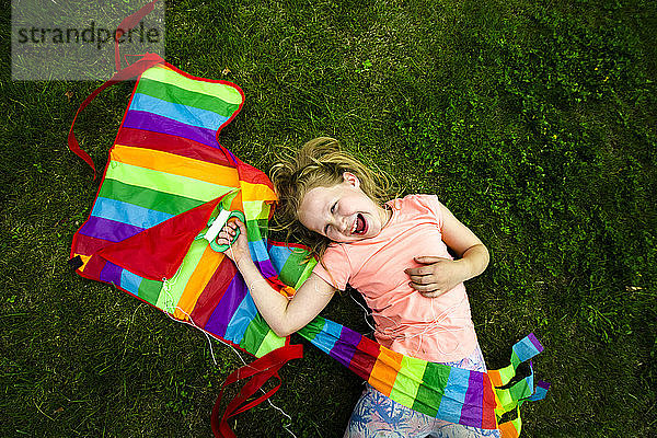 Glückliches Mädchen  das einen bunten Drachen hält  während es sich im Park hinlegt