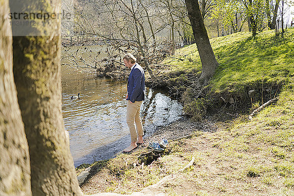 Männlicher Unternehmer steht am Flussufer im Park an einem sonnigen Tag