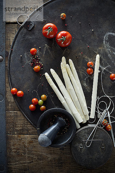 Mörser und Stößel  Pfefferkörner  Tomaten und geschälte Spargelstangen auf rustikalem Backblech