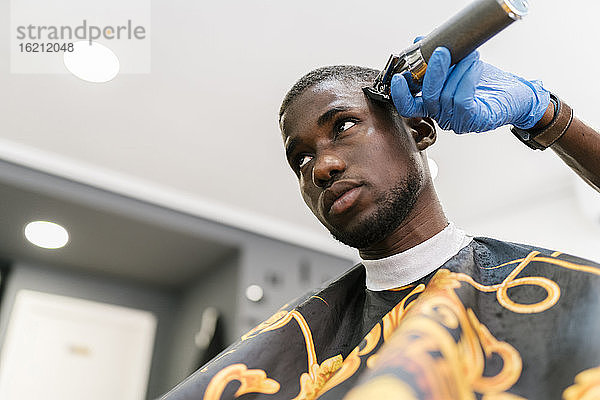 Ein männlicher Friseur mit Handschuh schneidet einem jungen Mann die Haare mit einem Rasiermesser