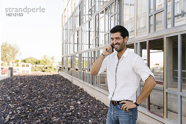 Lächelnder Geschäftsmann telefoniert vor einem Gebäude