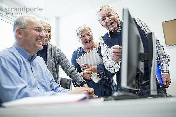 Aktive Senioren  die einen Computerkurs besuchen  den Kursleiter beobachten und sich Notizen machen