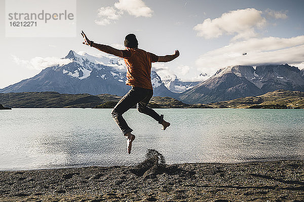 Mann mit ausgestreckten Armen beim Springen am Pehoe-See im Torres Del Paine National Park in Patagonien  Südamerika