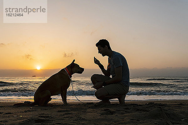 Mann spricht mit seinem Hund am Strand in der Morgendämmerung
