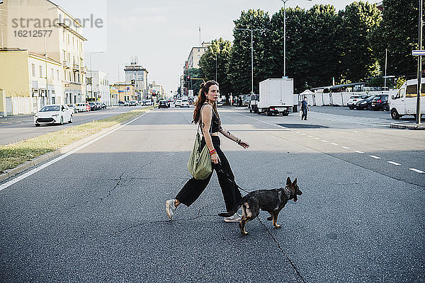 Frau überquert Straße mit Hund in der Stadt