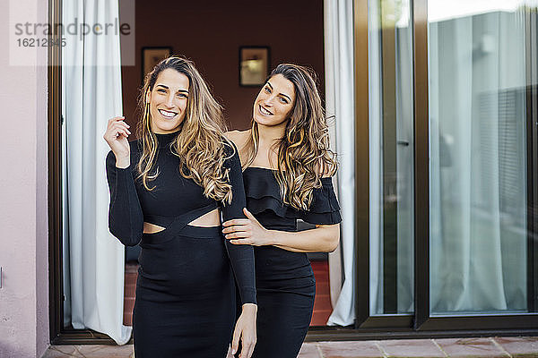 Lächelnde Zwillingsschwestern in Kleidern stehen im Freien an einem Touristenort