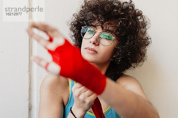 Nahaufnahme einer weiblichen Boxerin mit Afro-Haar  die sich im Fitnessstudio einen roten Verband um die Hand wickelt