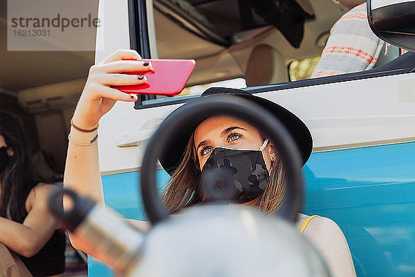 Frau mit chirurgischer Maske macht Selfie während einer Wohnmobilreise