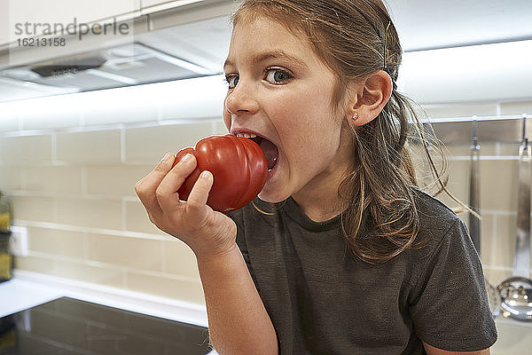 Nahaufnahme eines Mädchens  das eine Tomate isst  während es in der Küche zu Hause sitzt