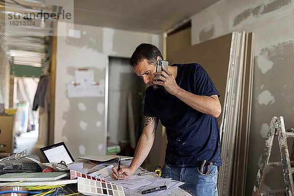 Mann am Telefon arbeitet an einem Bauplan