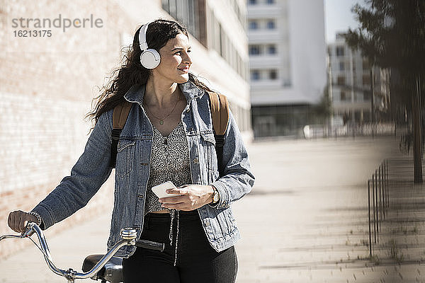 Junge Frau hört Musik und schaut weg  während sie mit dem Fahrrad in der Stadt steht