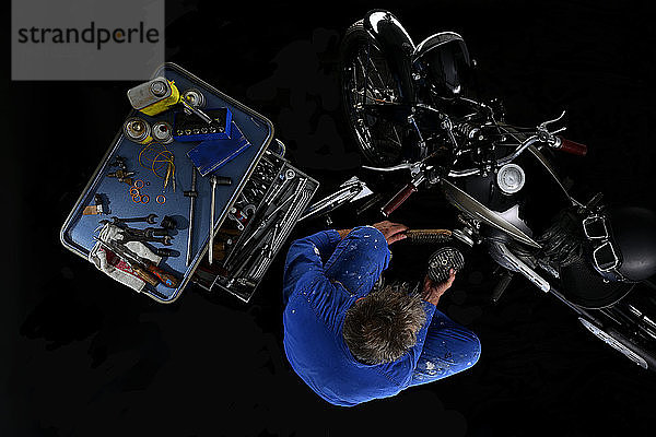 Draufsicht auf einen Mann  der ein altes Motorrad repariert  mit schwarzem Hintergrund (Ardie RZ)