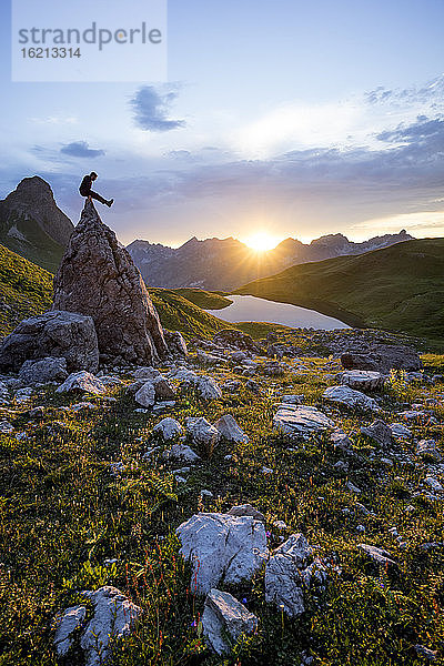 Wanderer sitzt bei Sonnenuntergang auf einem Felsen am Rappensee  Bayern  Deutschland