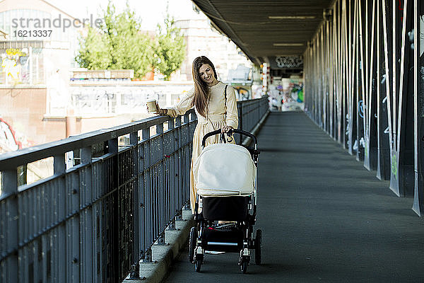 Lächelnde Mutter mit einem Kinderwagen auf einer Brücke