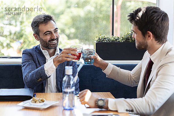 Geschäftsleute stoßen mit Getränken an  während sie am Tisch im Café sitzen