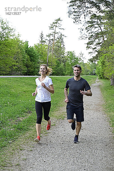 Glückliches Paar joggt auf unbefestigtem Weg gegen Bäume im Wald
