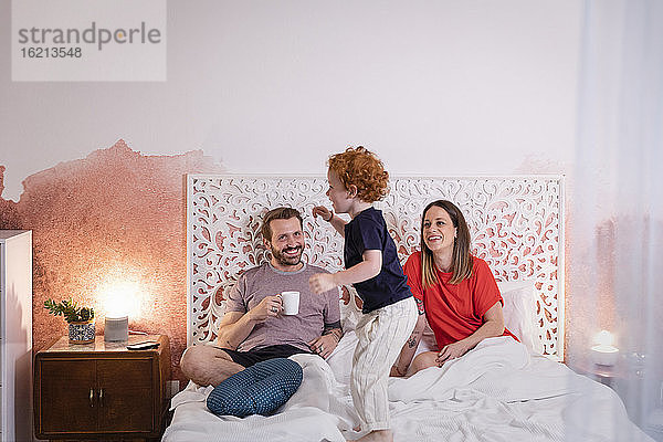 Eltern betrachten ihren verspielten Sohn beim Entspannen auf dem Bett
